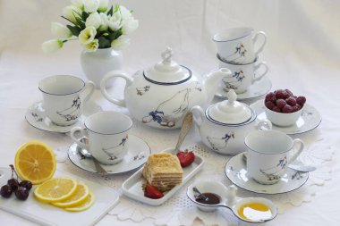 Lüks porselen çay seti ile bir bardak, Çaydanlık, süngerimsi pasta plaka ile beyaz masa örtüsü üzerinde şekerlik