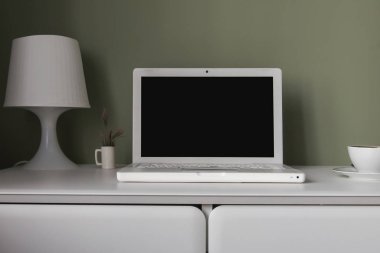 İskandinav tarzı - asılı tablo, beyaz dizüstü bilgisayar ve Resepsiyon lambası ve bir fincan çay yeşil duvar arka plan üzerinde beyaz işyerinde