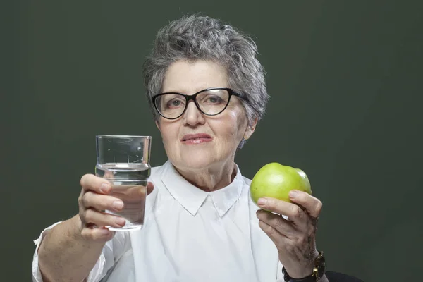 Healthy lifestyle, diet, healthy eating concept. Happy elderly woman holding a fresh green apple and a glass of water. Weight loss and youth