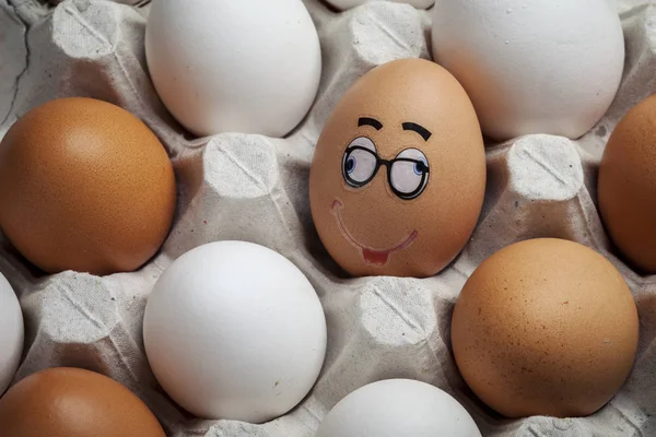 Funny egg with a face on the background of ordinary eggs in a carton. To be special