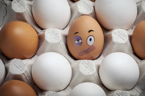 Funny egg with a face on the background of ordinary eggs in a carton. To be special