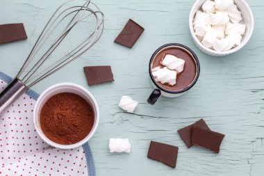 Mutfak eşyalarıyla çevrili mavi ahşap arka planda metal bir kupada lokum kaplı sıcak çikolata.