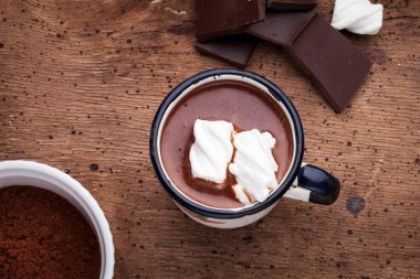 Demir bardakta sıcak çikolata, kasede kakao tozu, kırsal ahşap bir masada çırpı ve marşmelov.
