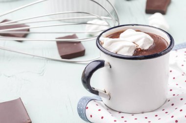 Mutfak eşyalarıyla çevrili mavi ahşap arka planda metal bir kupada lokum kaplı sıcak çikolata.