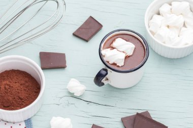 Mutfak eşyalarıyla çevrili mavi ahşap arka planda metal bir kupada lokum kaplı sıcak çikolata.
