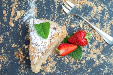 Siyah arka planda, çilek ve nane arkaplanlı, koyu arkaplanda bir parça kek Napolyon. Yukarıdan görünüm