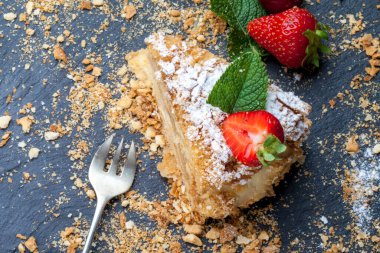 Siyah arka planda, çilek ve nane arkaplanlı, koyu arkaplanda bir parça kek Napolyon. Yukarıdan görünüm