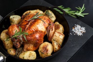 Fırında kızartılmış tavuk, patates dilimleri ve siyah arka planda dökme demir tavada taze biberiye. Yukarıdan görünüm
