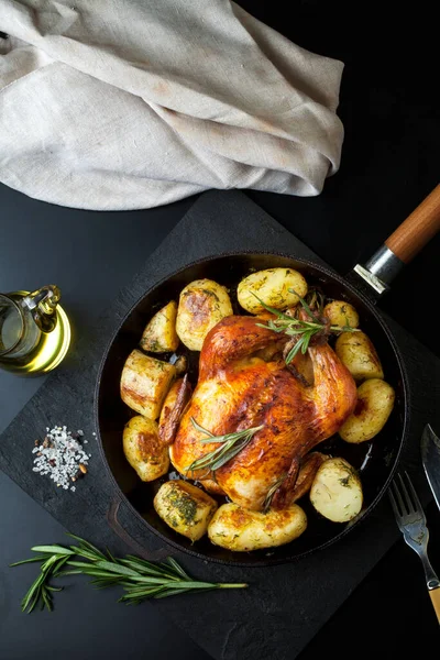 Fırında kızartılmış tavuk, patates dilimleri ve siyah arka planda dökme demir tavada taze biberiye. Yukarıdan görünüm