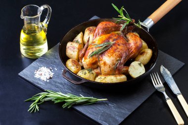 Fırında kızartılmış tavuk, patates dilimleri ve siyah arka planda dökme demir tavada taze biberiye. Yukarıdan görünüm