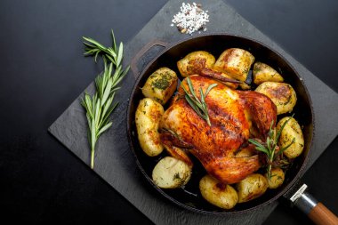 Fırında kızartılmış tavuk, patates dilimleri ve siyah arka planda dökme demir tavada taze biberiye. Yukarıdan görünüm