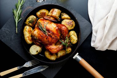 Fırında kızartılmış tavuk, patates dilimleri ve siyah arka planda dökme demir tavada taze biberiye. Yukarıdan görünüm