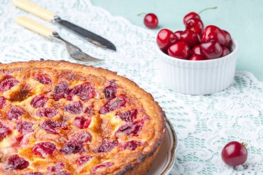 Arka planda bir kase kiraz olan vişneli turtayı bir tabağa koy.