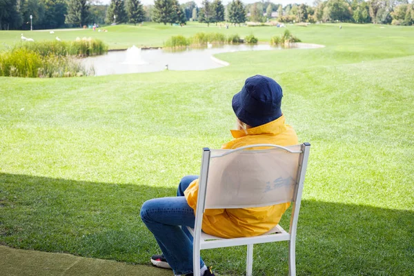 英国Kiev 2020年9月10日 一名身穿亮黄色夹克 头戴巴拿马帽的女子在阳光灿烂的一天结束后坐在一个绿色高尔夫球场上 背景色 — 图库照片