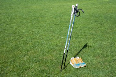 Kiev, Ukrayna - 10 Eylül 2020: İskandinav yürüyüş ekipmanları. Parktaki yeşil çimlerin arka planına yakın çekim çubukları ve spor ayakkabıları. Aktif ve sağlıklı yaşam tarzı.