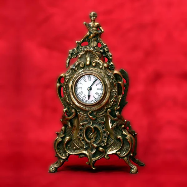 Antika bir şekilde dekore edilmiş bronz saat kırmızı kadife arka plan üzerinde