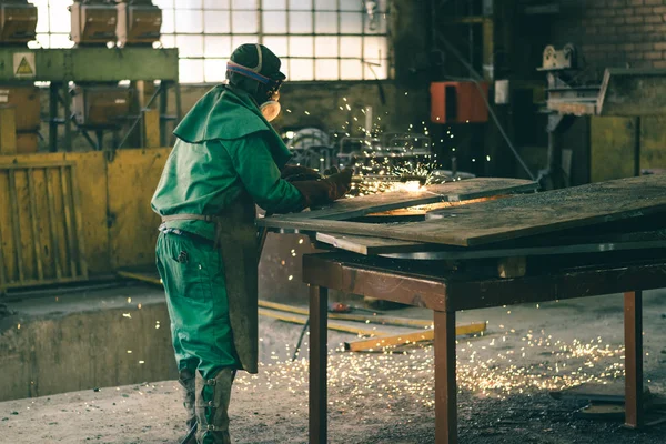 A foundry metal worker cutting through sheet of metal with a blow torch