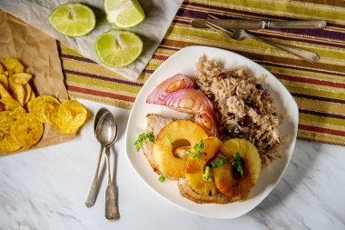 Marinated Cuban pineapple pork chops with traditional black bean rice grilled red onion and fried plantain chips clipart