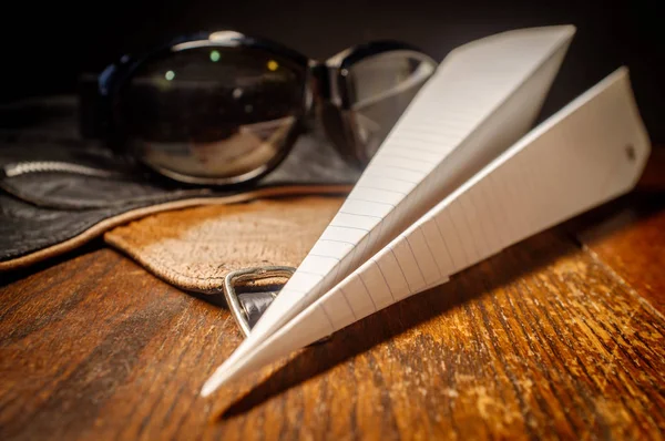 アビエイター の帽子ゴーグルと素朴な木製のテーブル上の紙飛行機 — ストック写真