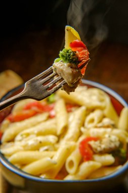 Izgara tavuk alfredo penne primavera rustik ahşap mutfak masasında karanlık moody aydınlatma ile