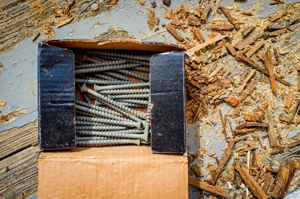 Box of contracting deck screws with sawdust on worn wooden porch