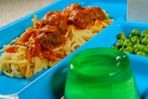 Grade school lunch tray of Italian spaghetti and meatballs with green peas milk carton and gelatin