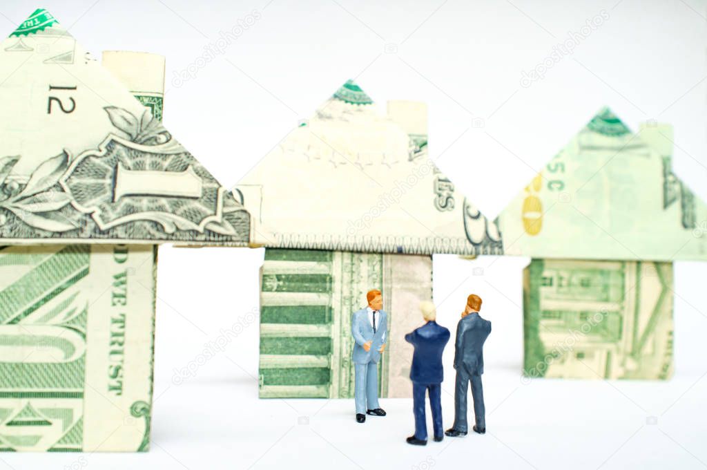 Miniature figurine businessmen and origami paper money houses for real estate and housing market concept