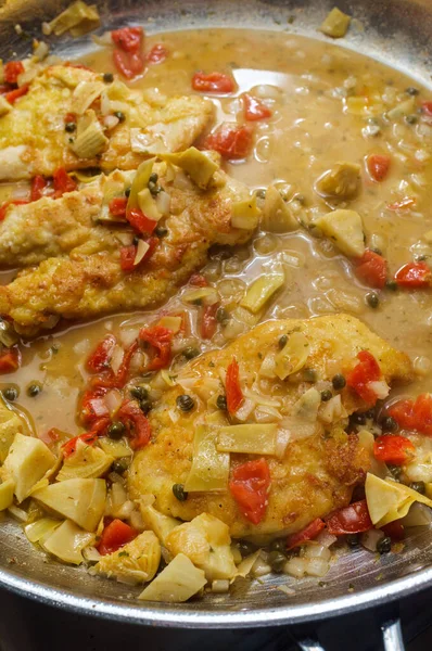 Italian chicken piccata with artichoke hearts and capers cooking in large pan