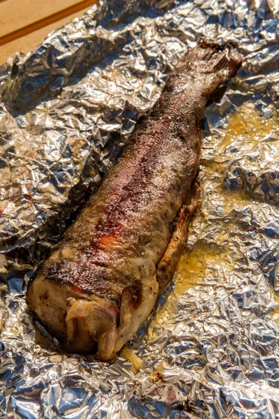 Skin-on grilled trout in aluminum foil after being cooked at an outdoor barbecue