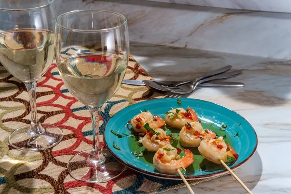 Romantic dinner Portuguese gambas al ajillo garlic shrimp on skewers with two glasses of pinot grigio white wine