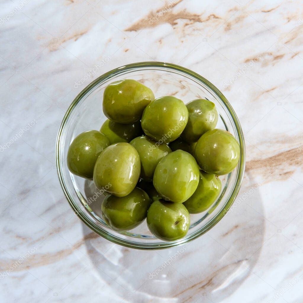 Nocellara del Belice or castelvetrano olives in glass bowl on marble kitchen table