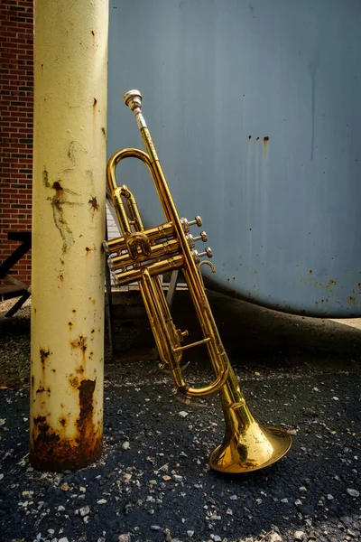 Abandoned old rusty Jazz trumpet leaning against yellow pillar on city street outside club