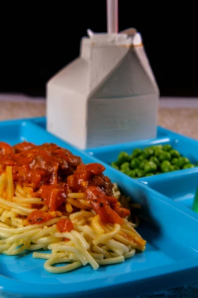 Grade school lunch tray of Italian spaghetti and meatballs with green peas milk carton and gelatin