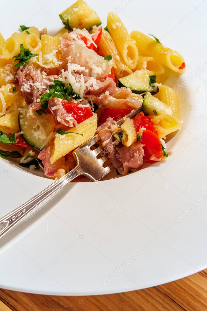 Gourmet Italian penne pasta with tomatoes zucchini and prosciutto garnished with grated asiago cheese and parsley