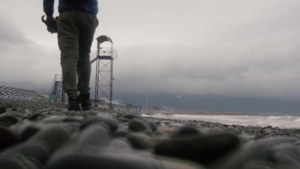 Mężczyzna w butach trekkingowych idzie w kierunku wieży. Pusta Jesienna plaża. — Wideo stockowe