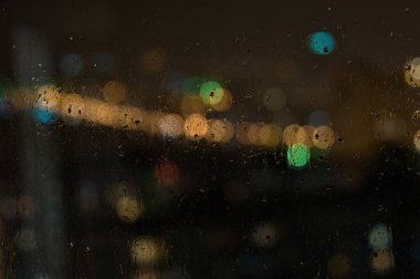 Şehirde gece penceredeki yağmur damlalarının görüntüsü.