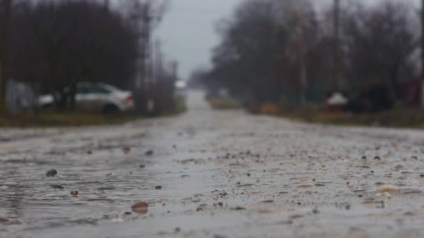 Férfi fut fedezékbe keresztül kavicsot műút, esős napon, míg a háttérben nedves úton autó-meghajtók. — Stock videók