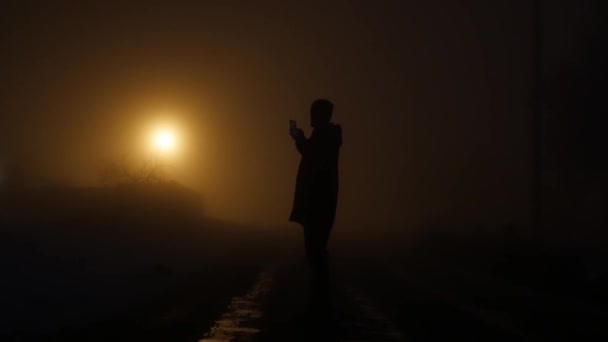 Lage hoekmening van man smartphone kijken in donkere nacht. mystieke mist achtergrond. lichtstralen — Stockvideo