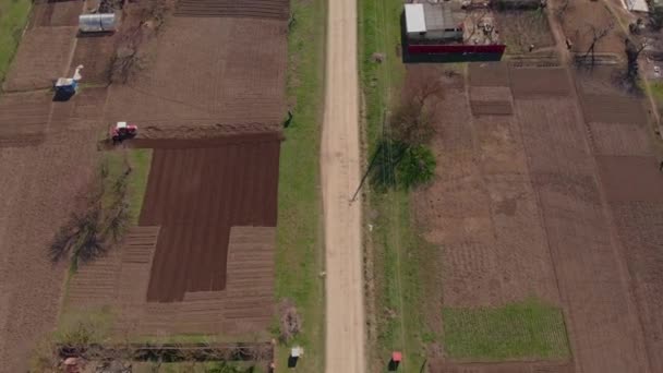 A small tractor plows the land in the village, shooting from a drone from different angles. The beginning of the plowed season, early spring, the beginning of planting vegetables — Stock Video