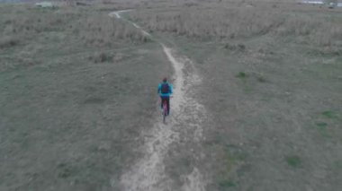 bir telefon ve bir sırt çantası ile bisikletçi Park geçer, bir eşlik ile bir drone çekim.
