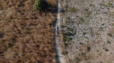 Bir bisiklet bisikletçi kuru çim arasında parkta sürmek. Yalnız bisiklet ışık seyahat kavramı. Drone çekim