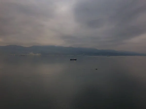 El barco está anclado en tiempo nublado y brumoso contra el telón de fondo de las montañas, tiempo lluvioso, temprano en la mañana —  Fotos de Stock