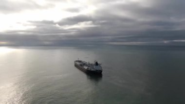 Hava görüntüsü kargo gemisini demirliyor. Suyun üzerinde uçan insansız hava aracı bulutlu bir günde, çapadaki yalnız tankerin etrafında deniz manzarası gösteriyor.