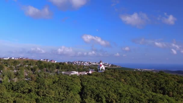 Vista panorâmica aérea de uma igreja no topo de uma montanha com áreas verdes, floresta, baía, mar, montanhas, cemitérios e casas ao fundo — Vídeo de Stock