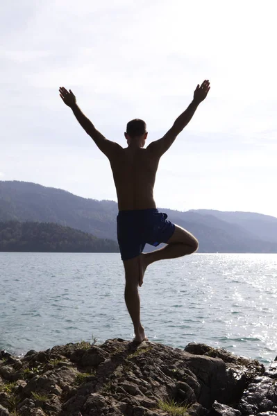Man practicing yoga outside near a lake in the morning