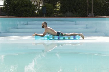 Genç bir adam ve yüzücü boş bir havuzda şişme yatakta.