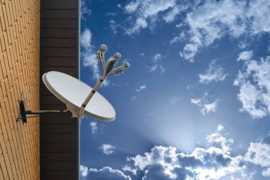 Mavi gökyüzü arka planındaki özel bir evin duvarına uydu anteni monte edilmiş.