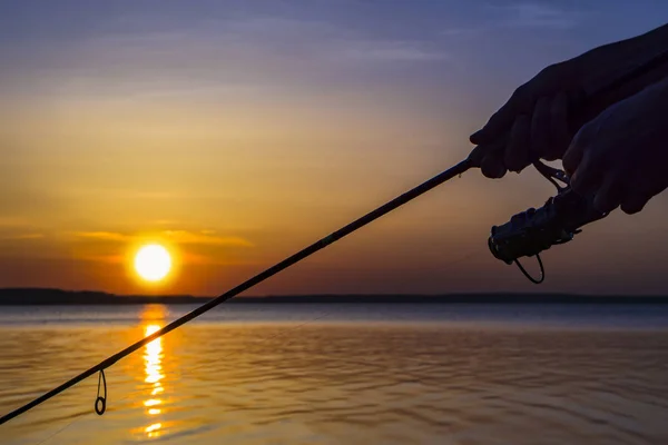 Silhouette der Hände des Fischers mit Angelrute auf dem Hintergrund des Sonnenuntergangs — Stockfoto