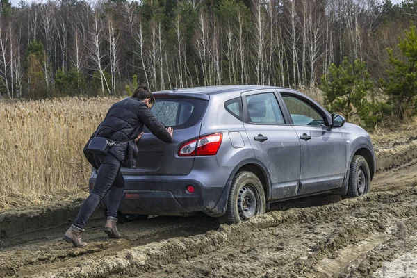 Chica empujando coche atascado en camino de tierra pantano — Foto de Stock