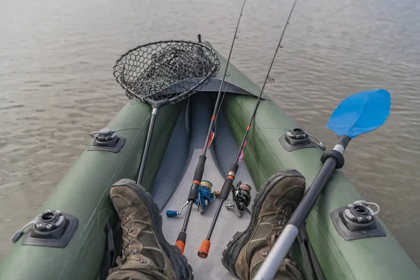 Kayak fishing at lake. Legs of fisherman on inflatable boat with fishing tackle.